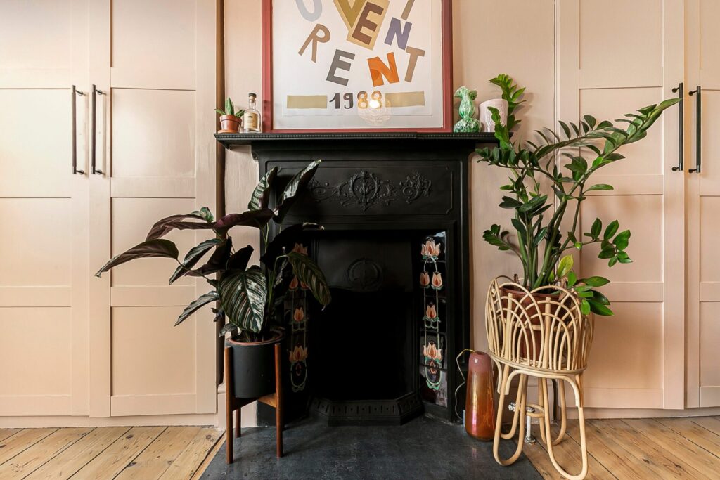 Interior view of a Victorian-style black fireplace decorated with lush green plants, set against neutral pink walls and custom fitted cabinetry.
